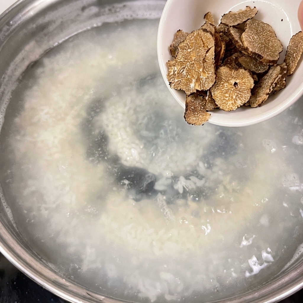 Eine kleine weiße Schüssel mit Trüffelscheiben wird in einen Topf mit simmerndem Wasser gegeben.