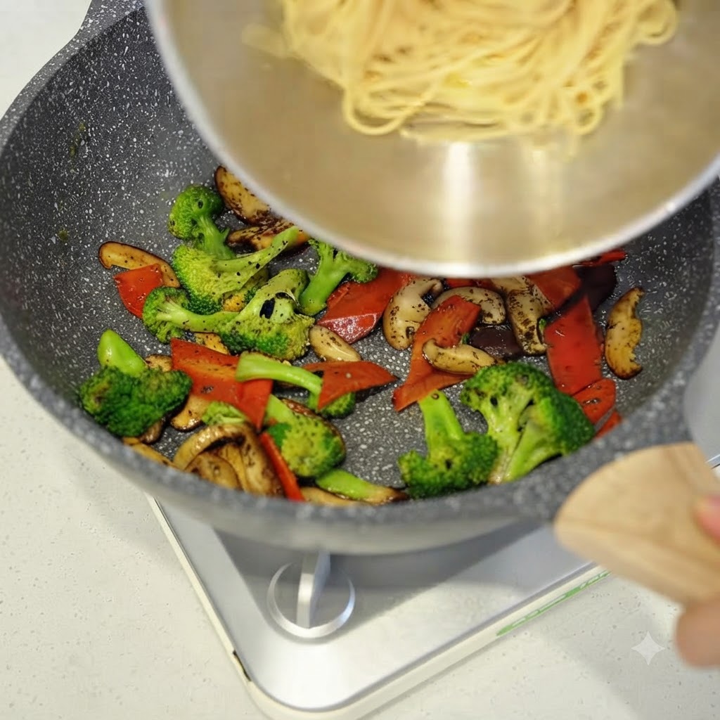 Gekochte Spaghetti werden aus einer Schüssel in die Pfanne mit dem angebratenen Gemüse gegeben.