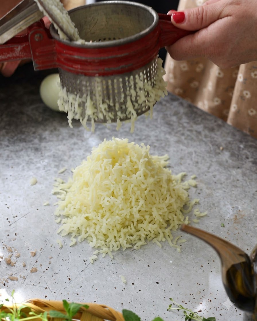 Heiße gekochte Kartoffeln werden durch eine rote Kartoffelpresse zu einem fluffigen Haufen auf dem Tisch gedrückt.