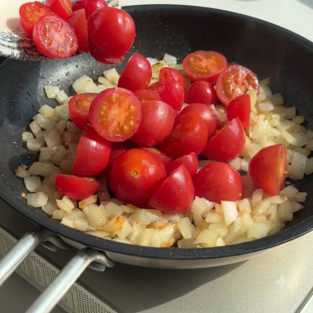 Halbierte Kirschtomaten werden in die Pfanne mit Zwiebeln und Knoblauch gegeben und verrührt.