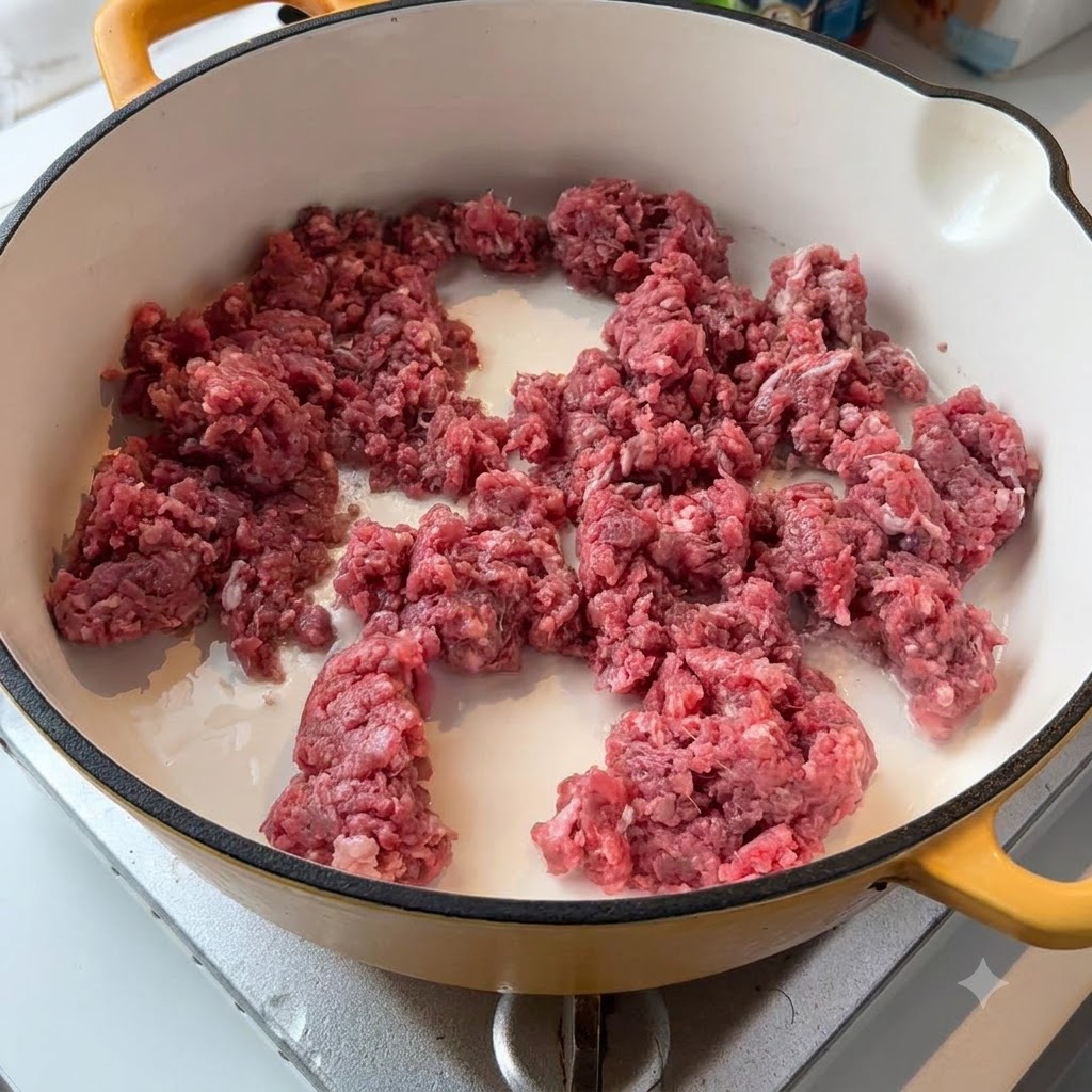 Rohes Rinderhackfleisch und weiße Zwiebeln brutzeln in einer hellen Pfanne auf dem Herd.