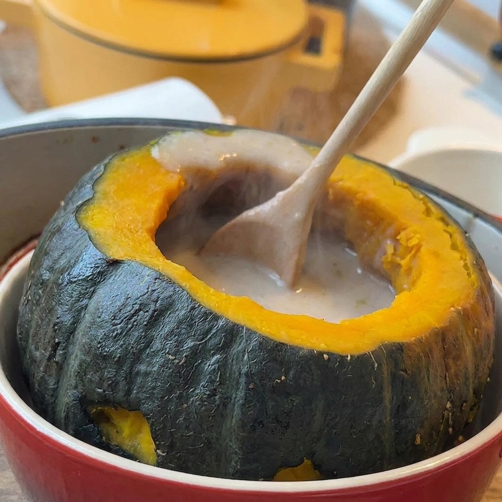 Heiße cremige Suppe wird mit einem Schöpflöffel in einen ausgehöhlten Minikürbisbehälter gefüllt.