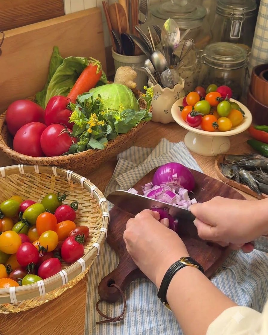 Eine Hand schneidet mit einem Messer Kirschtomaten auf einem Holzschneidebrett in Hälften.