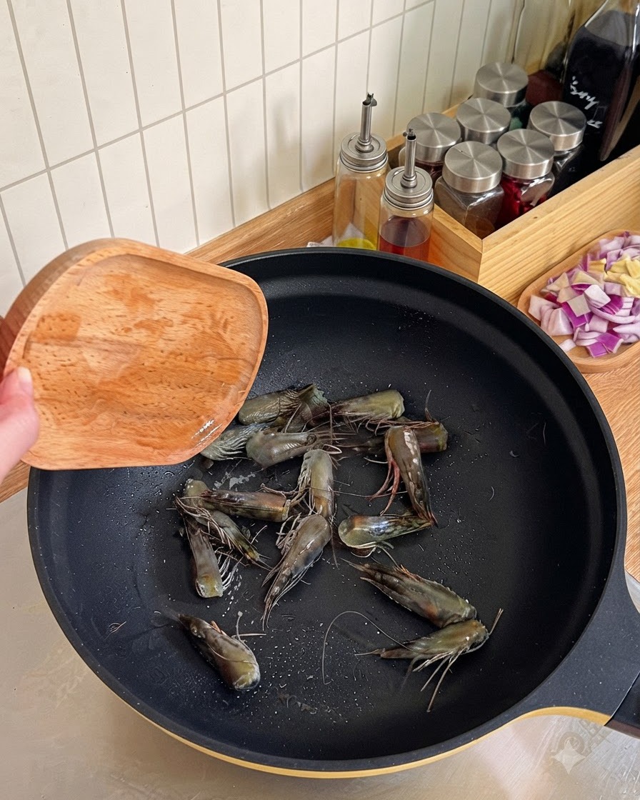 Garnelenköpfe werden in einem schwarzen Wok angebraten und mit einem Holzspatel ausgedrückt, um Öl zu gewinnen.