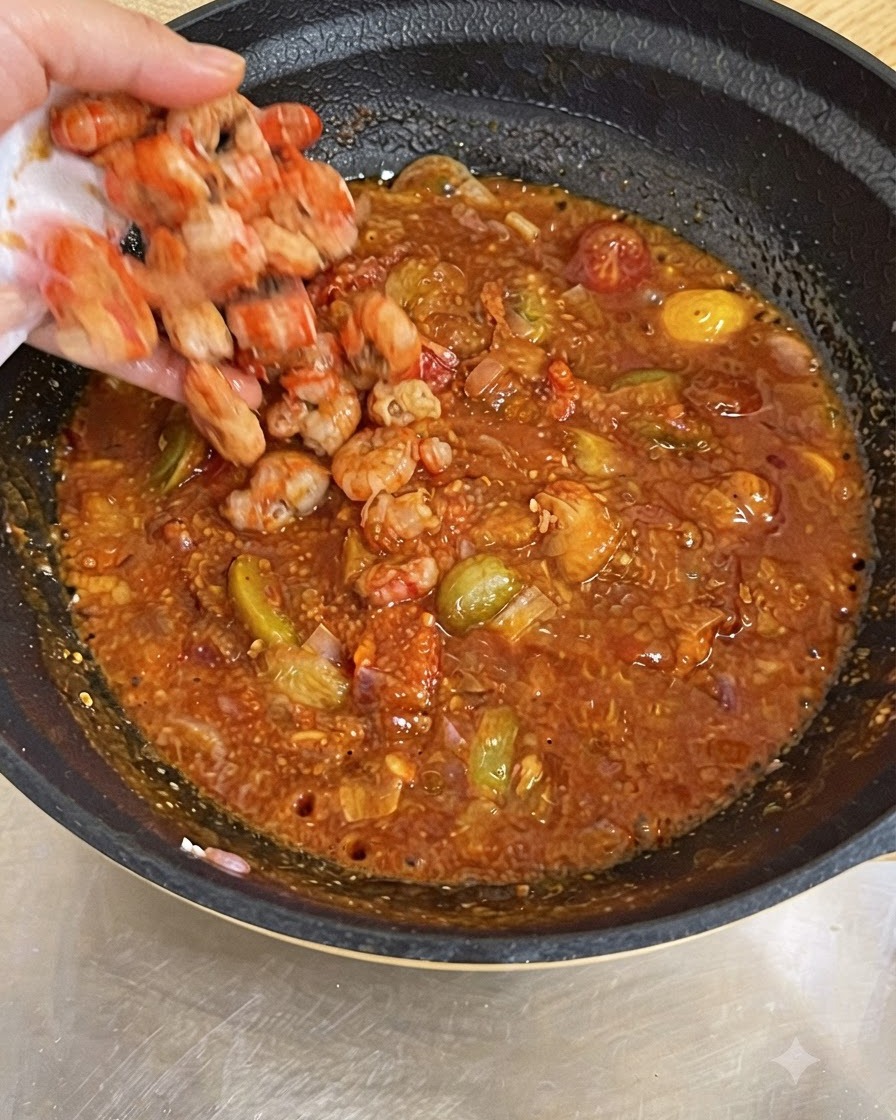 Eine Hand wirft gekochte Garnelen in eine Pfanne mit blubbernder roter Tomatensauce.
