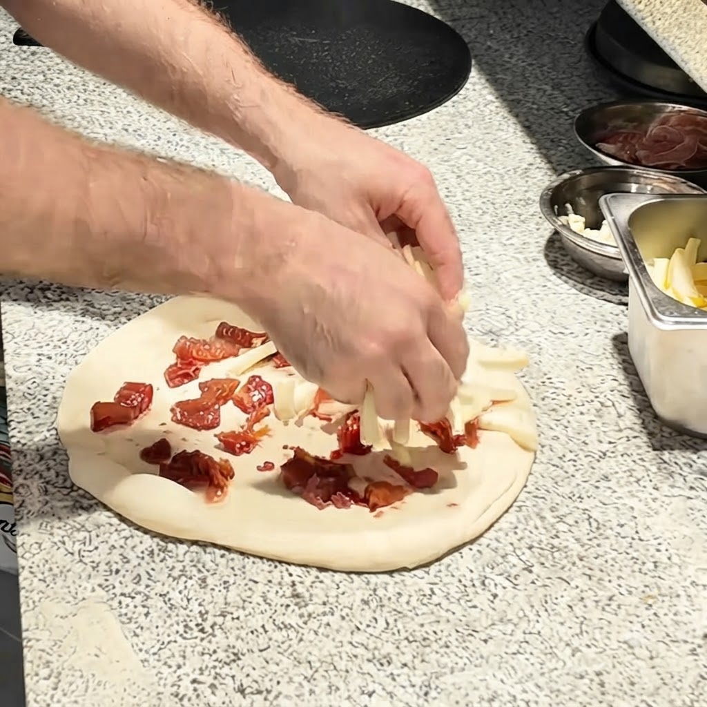 Mozzarellastreifen werden über die Tomatenschicht auf dem Pizzateig gestreut.