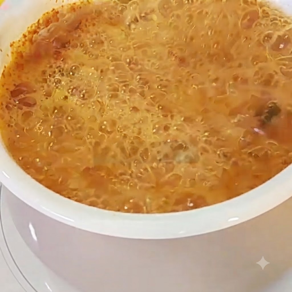 Ein Ei wird in einen Topf mit blubbernder roter Ramen-Brühe geschlagen.