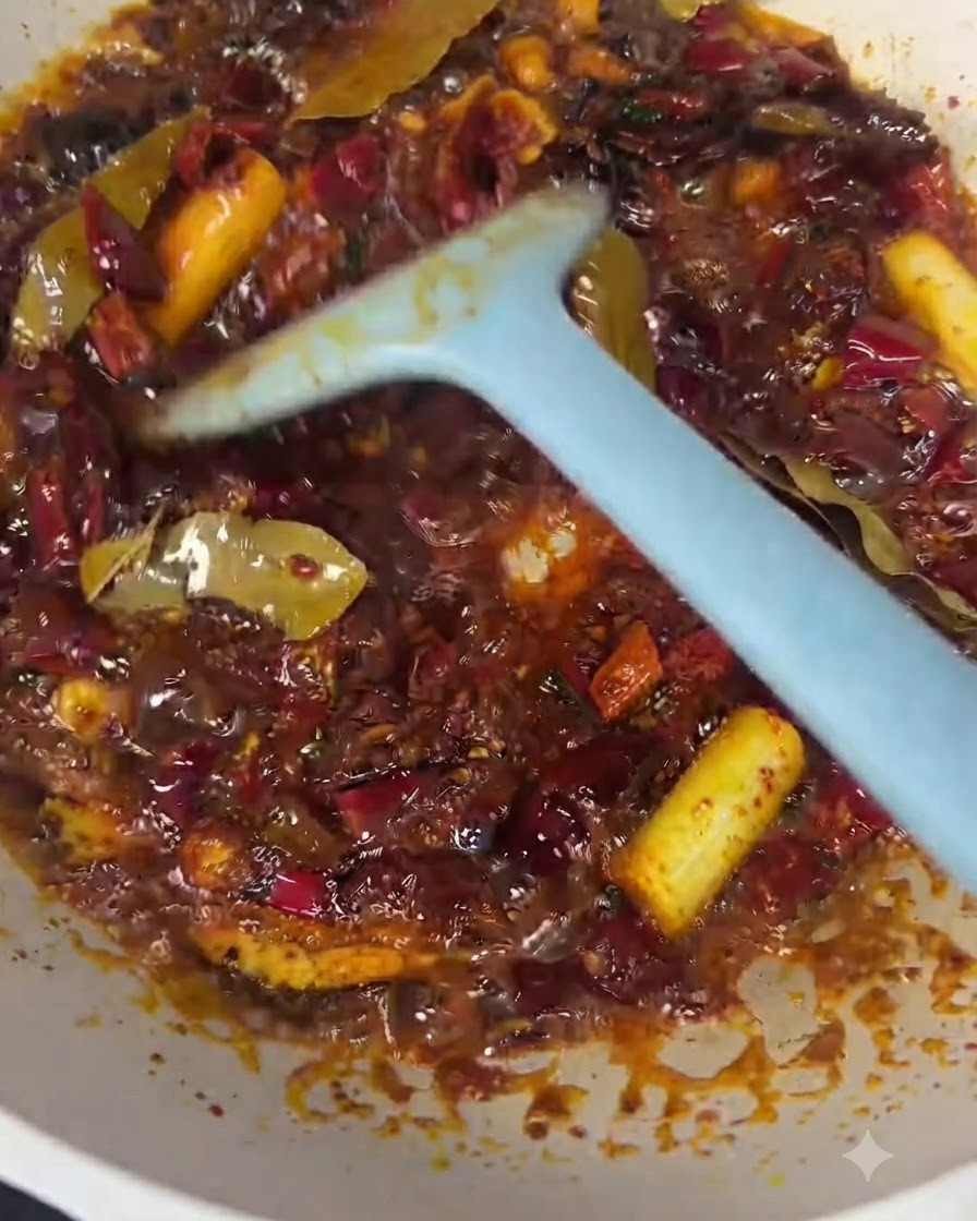 Rindfleischstücke werden mit einem blauen Pfannenwender in das rote Chiliöl und die Gewürzbasis gemischt.