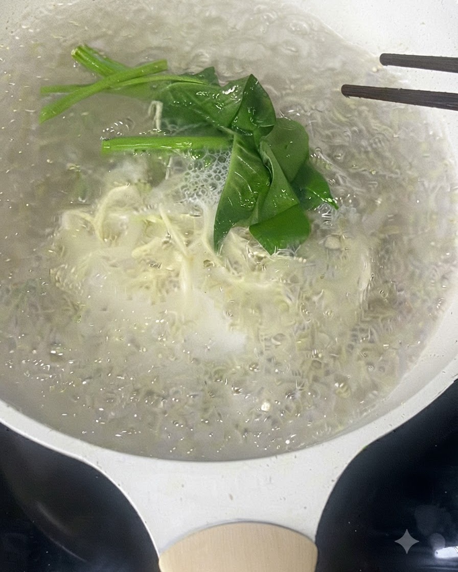 Essstäbchen rühren dünne weiße Nudeln und grünes Blattgemüse in kochendem Wasser um.