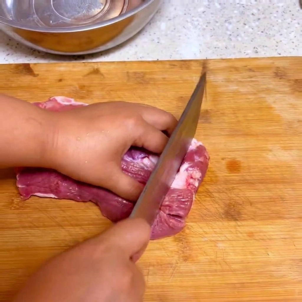 Ein Küchenmesser schneidet frisches, rohes Rindfleisch auf einem Holzschneidebrett in große Stücke.