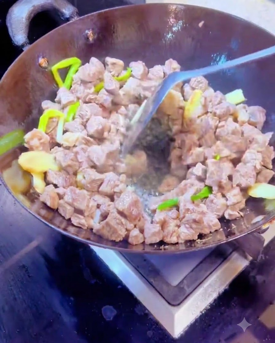 Trockene Gewürze und Rindfleischwürfel werden mit einem Metallspatel in einem heißen Wok vermengt.