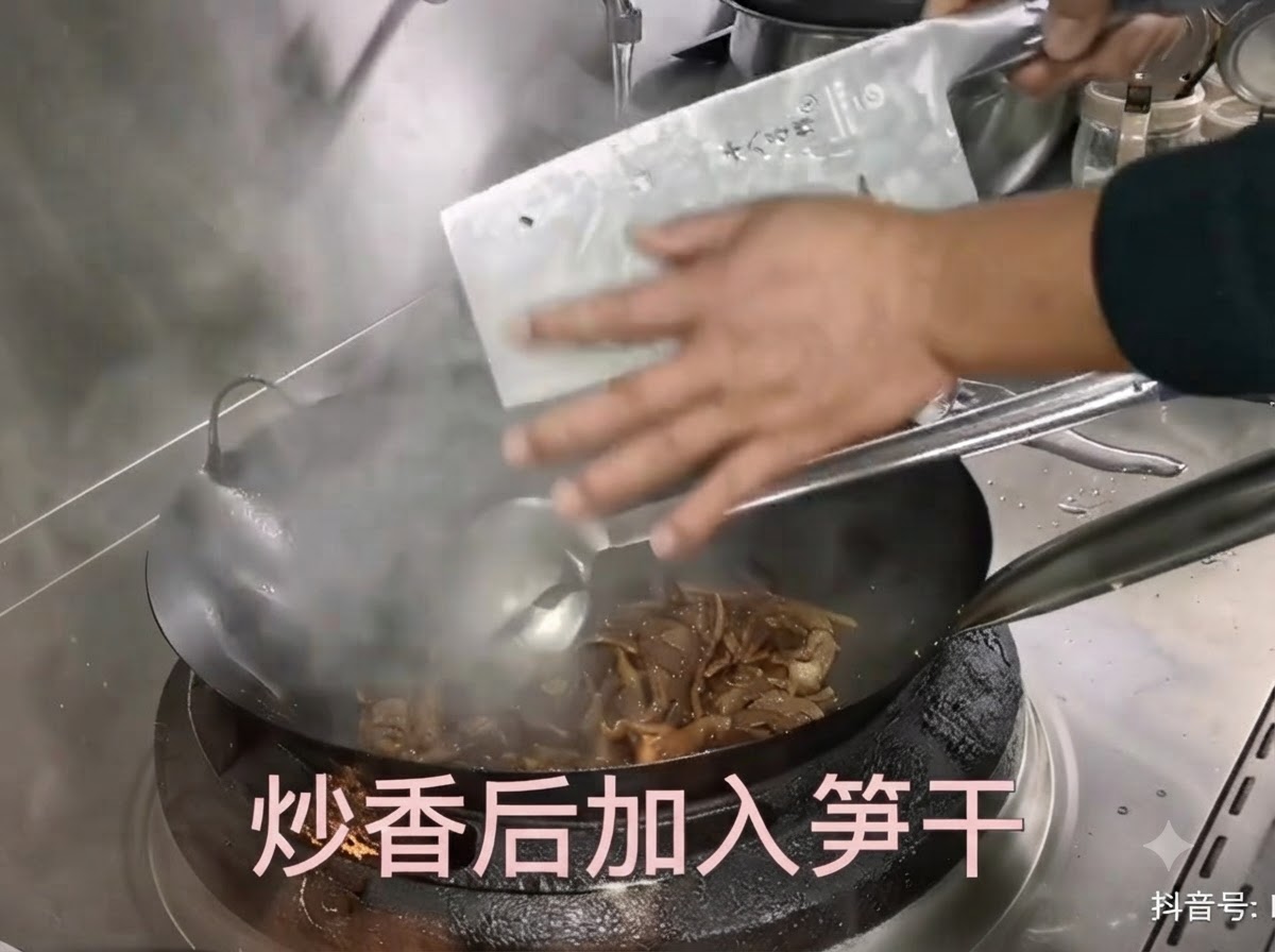 Vorbereitete getrocknete Bambussprossen werden von einem Beil in einen heißen Wok mit anbratendem Fleisch geschabt.