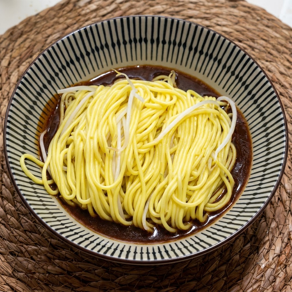 Eine Portion heißer, gekochter gelber Nudeln liegt in einer gemusterten Keramikschüssel auf einer cremigen, dunkelbraunen Sauce.