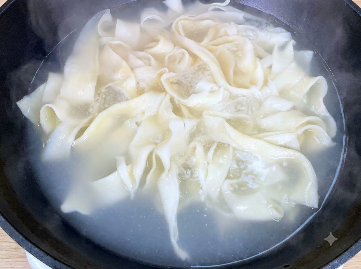 Frischer Baby-Pak-Choi kocht zusammen mit breiten Nudeln in einem Topf.