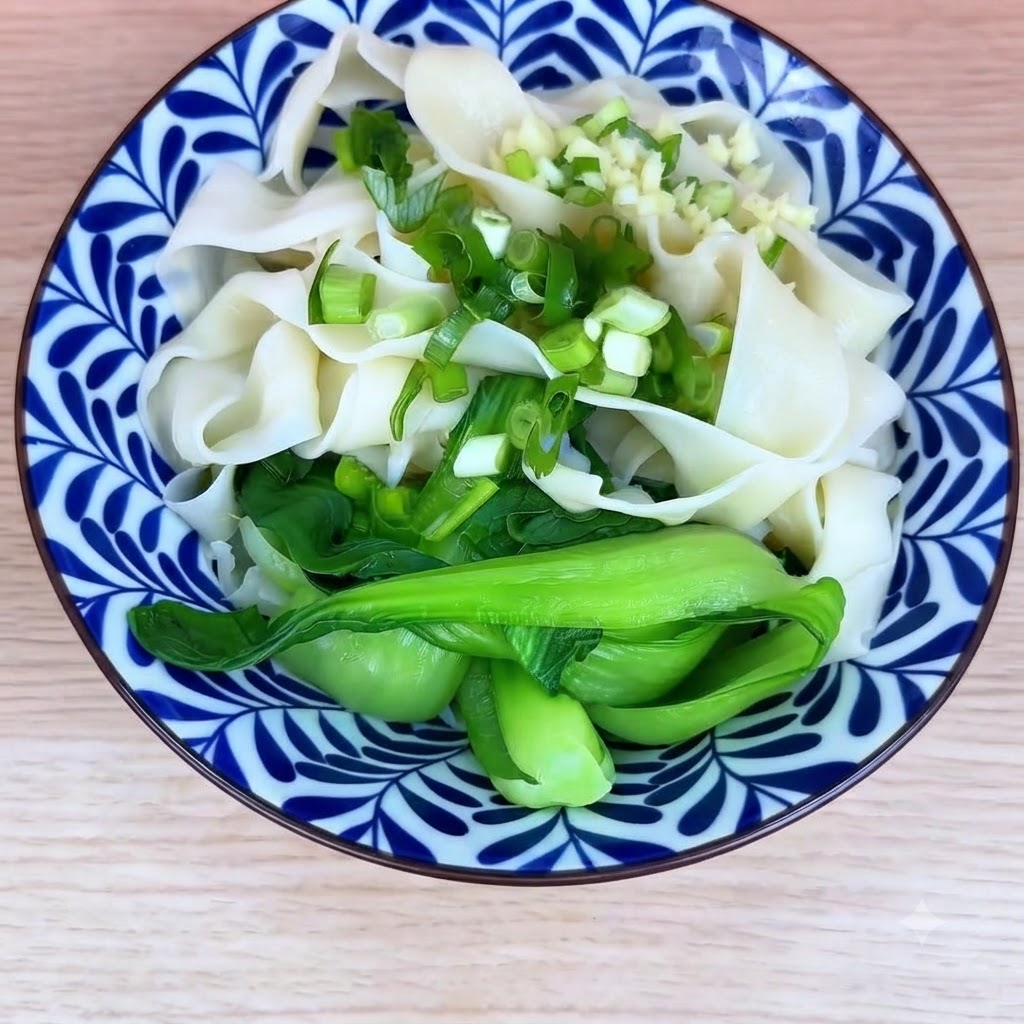 Eine Schüssel mit gekochten Nudeln und Pak Choi, getoppt mit gehackten Frühlingszwiebeln und Knoblauch.