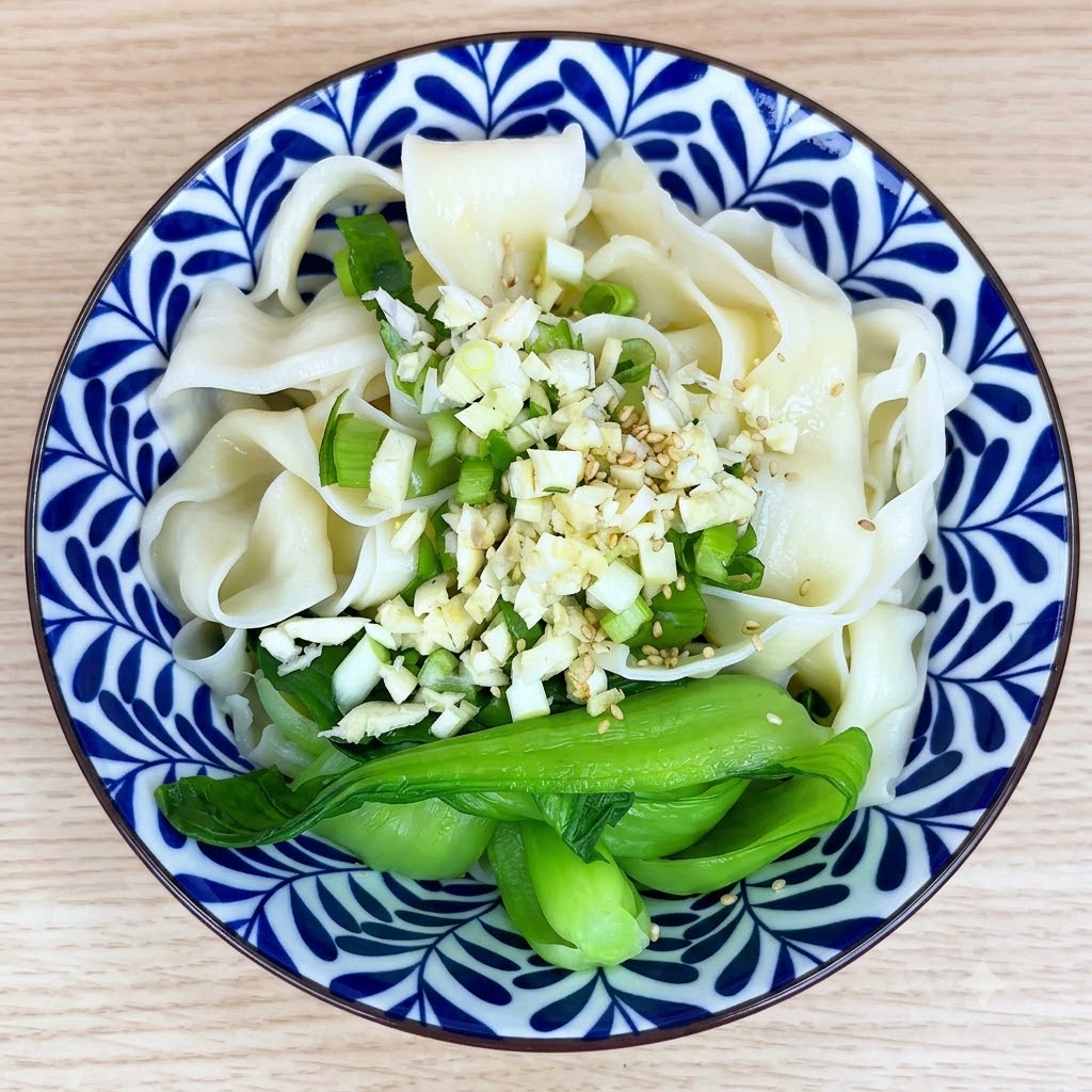 Weiße Sesamsamen und Gewürze sind auf dem Knoblauch und den Nudeln in einer Schüssel verstreut.