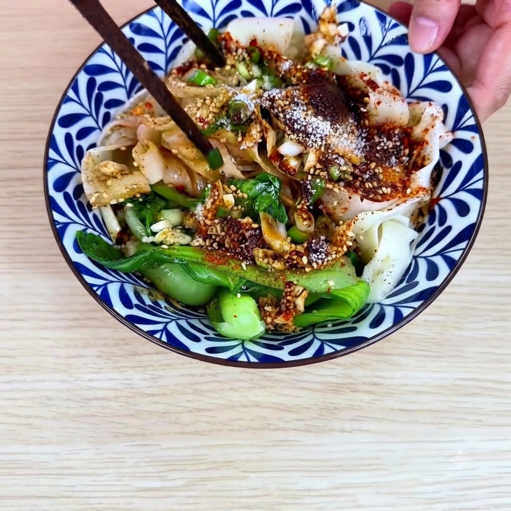 Essstäbchen vermischen die breiten Weizennudeln, den Pak Choi und die Chili-Öl-Sauce in der Keramikschüssel.