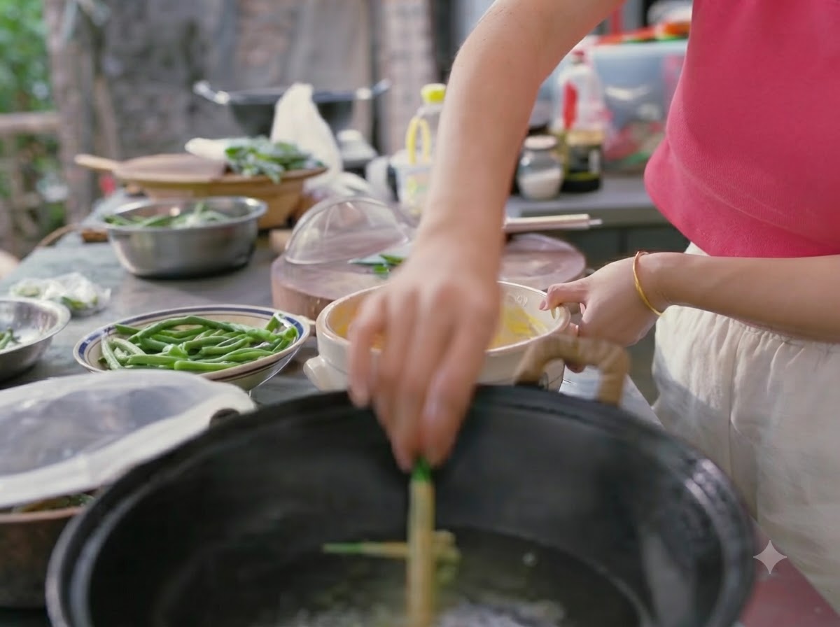 Eine Hand senkt teigummantelte grüne Bohnen in einen Wok mit kochendem Wasser.
