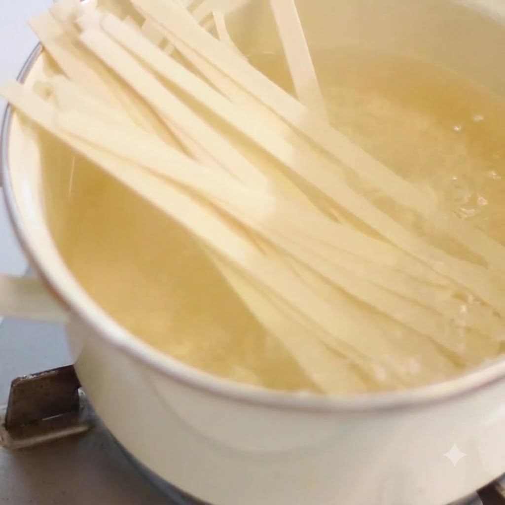 Breite Nudeln kochen in einem Topf mit kochendem Wasser auf einem Herd.