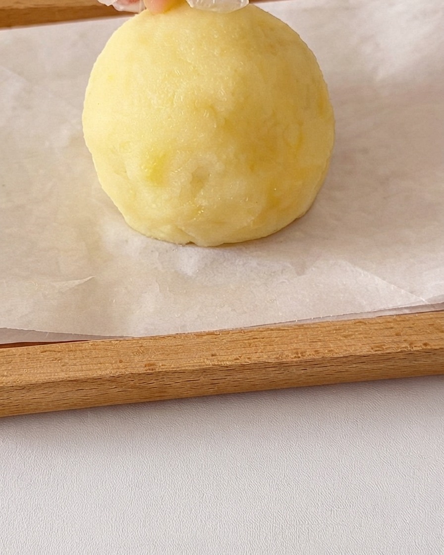 Eine runde Kugel aus glattem Kartoffelpüree wird mit Händen geformt, wobei kleine Kartoffelstücke oben für Ohren hinzugefügt werden.
