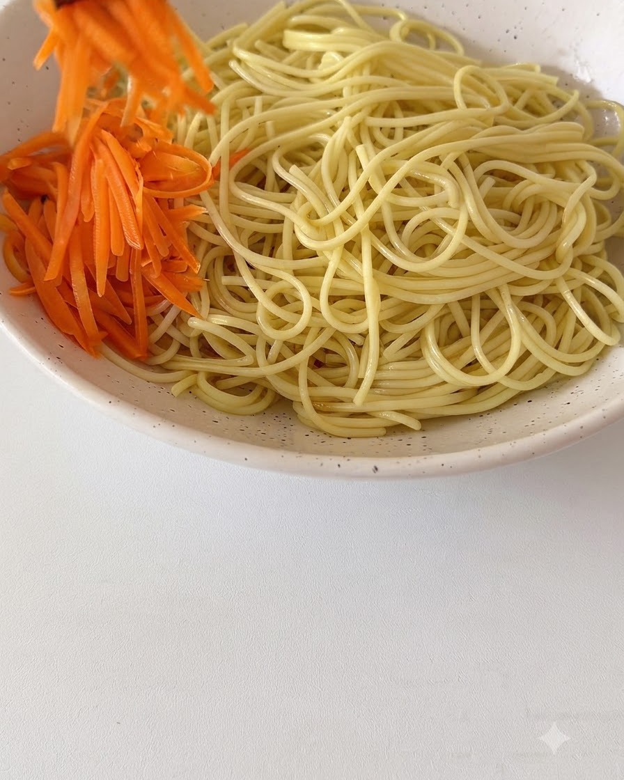 Frische geraspelte Karotten und andere Toppings werden auf den gekochten Nudeln in einer großen Keramikschüssel arrangiert.
