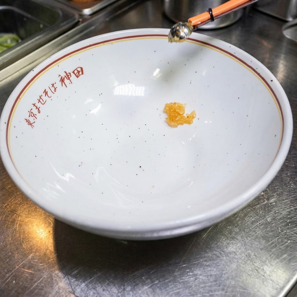 Eine kleine Menge Würzflüssigkeit am Boden einer leeren weißen Schüssel mit japanischem Text.