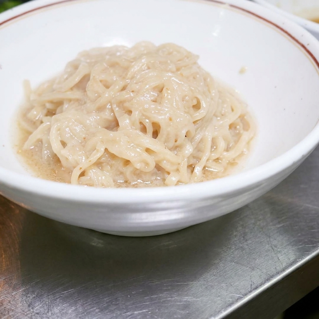 Gekochte Ramen-Nudeln liegen ordentlich in einer weißen Schüssel und warten darauf, mit der Sauce vermischt zu werden.