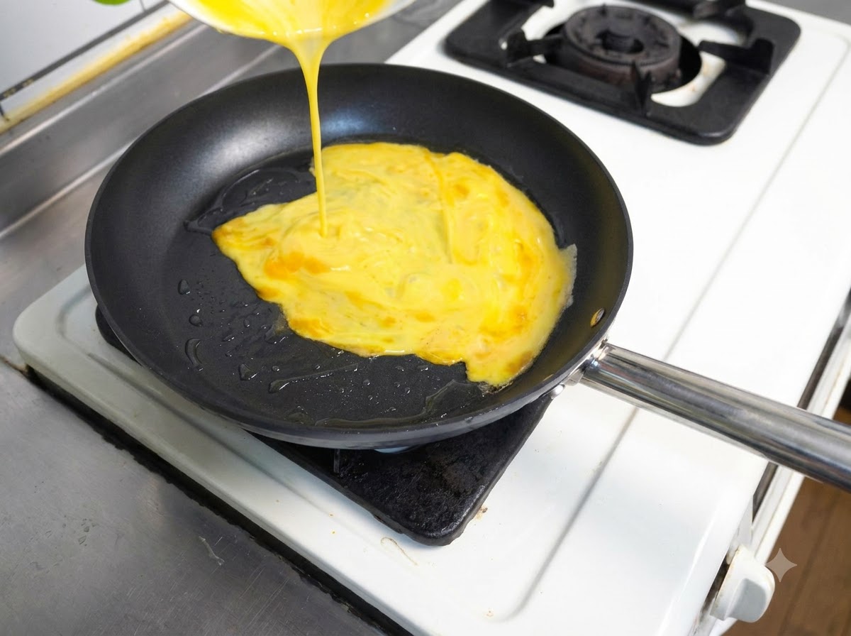 Verquirlte gelbe Eier werden aus einem Behälter in eine heiße Bratpfanne mit Öl gegossen.