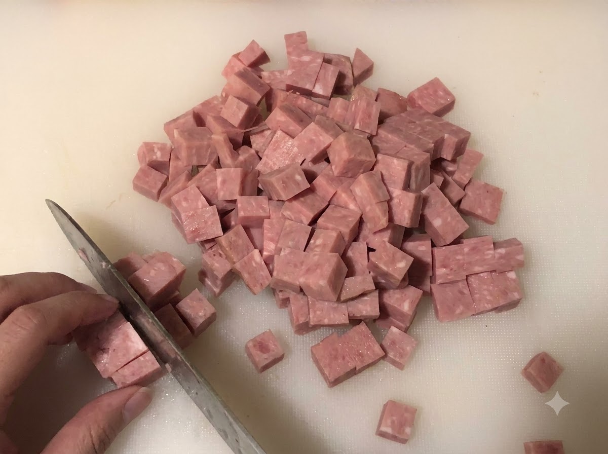 Spam wird auf einem Schneidebrett in kleine Würfel geschnitten, mit gehackten Zwiebeln und Frühlingszwiebeln im Hintergrund.