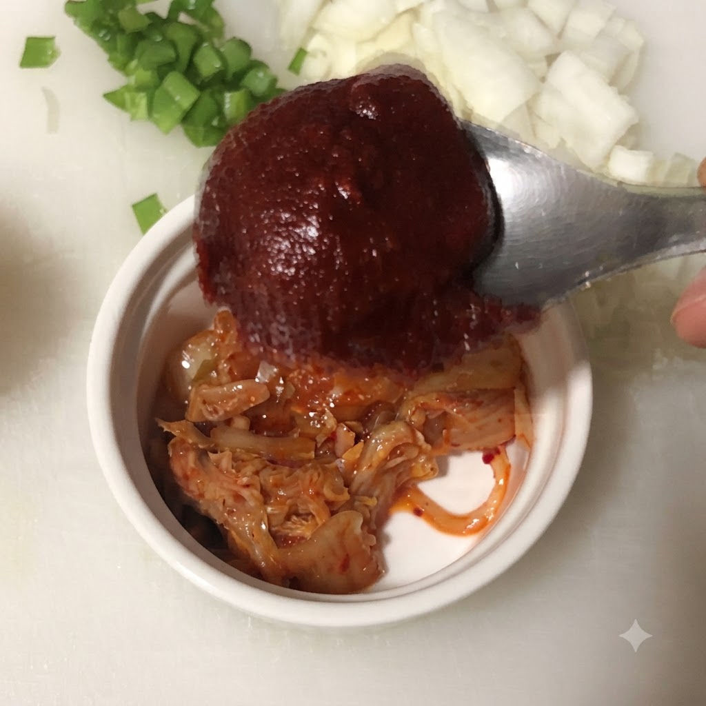 Ein Löffel koreanische Chilipaste wird über eine Schüssel mit gehacktem Kimchi gehalten.