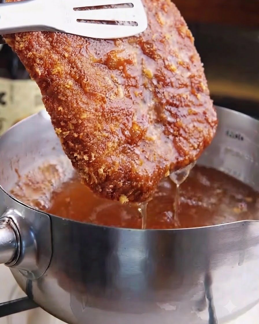 Ein knuspriges, goldbraun frittiertes Schweineschnitzel wird mit einer Zange aus dem heißen Frittieröl gehoben.