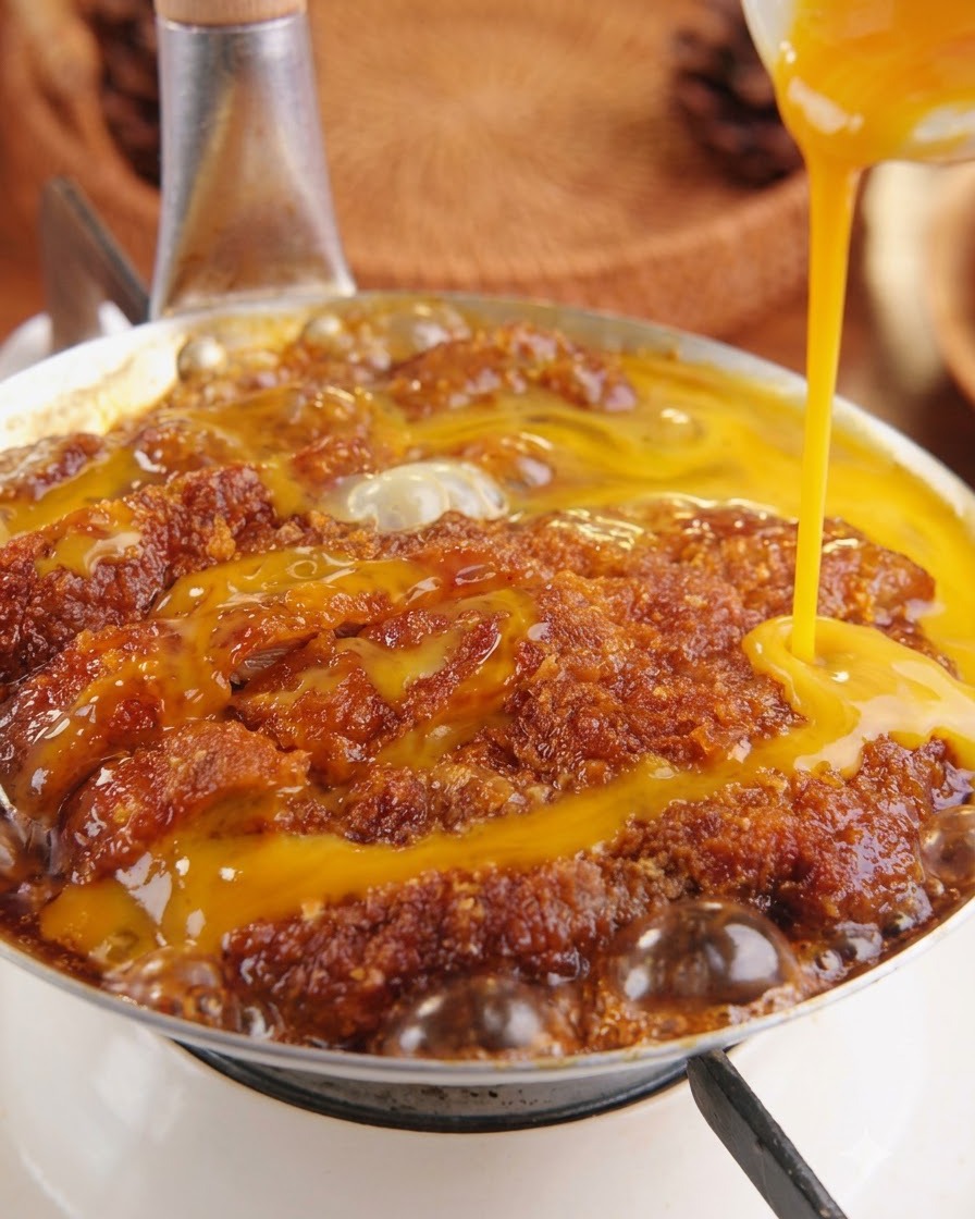 Gelbe, verquirlte Eimasse wird von oben auf das köchelnde Schweineschnitzel in einer Pfanne gegossen.