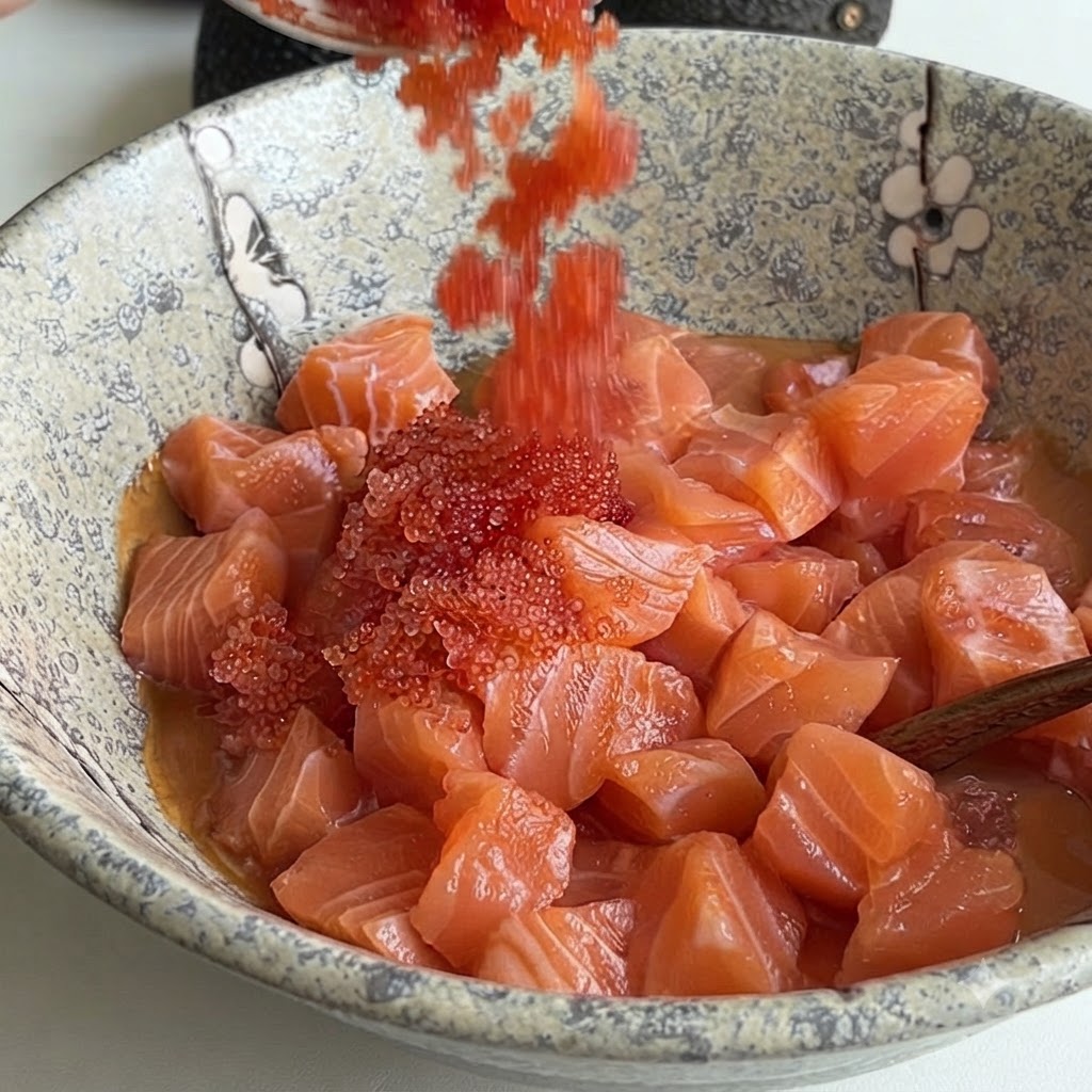Hellroter Fischroggen wird von einem Löffel in eine Keramikschüssel mit gewürfeltem Lachs und Soße gegeben.