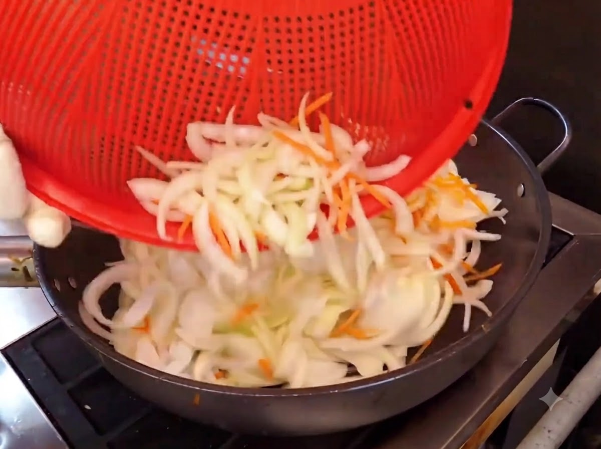 Zwiebel- und Karottenstreifen werden aus einem roten Korb zum Anbraten in einen heißen Wok gegeben.