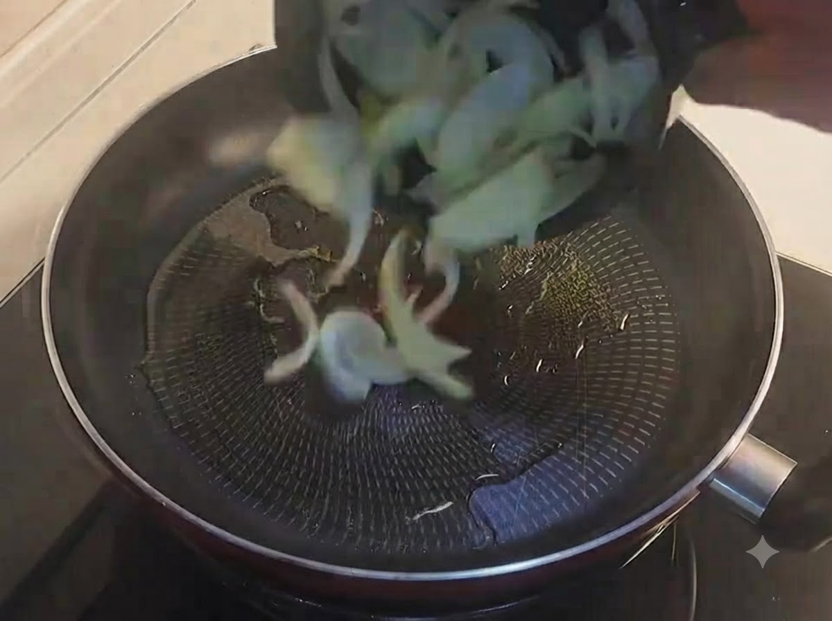 In Scheiben geschnittene gelbe Zwiebeln werden in eine geölte schwarze Bratpfanne gegeben.