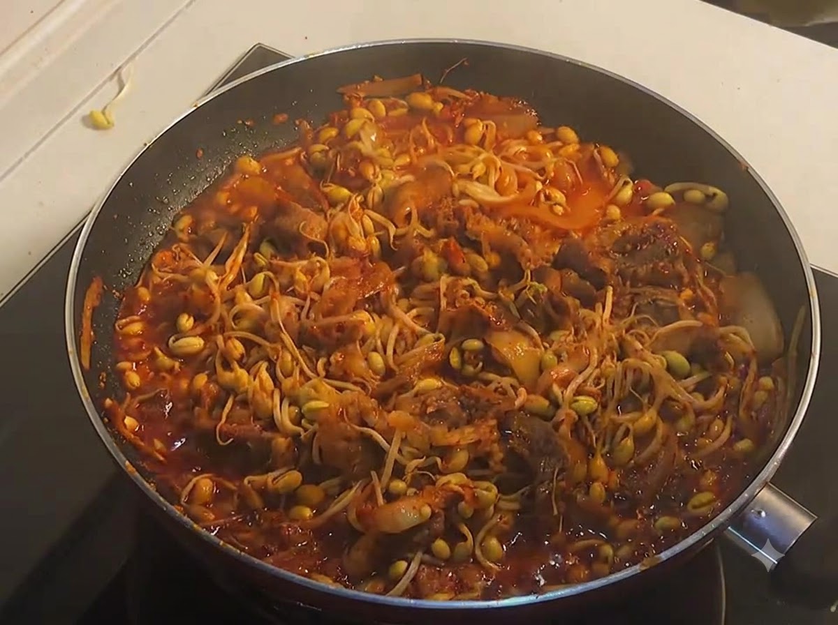 Eine Pfanne voller fertig gekochtem, blubberndem scharfen Rindfleisch und gelben Sojasprossen in einer reichhaltigen roten Sauce.