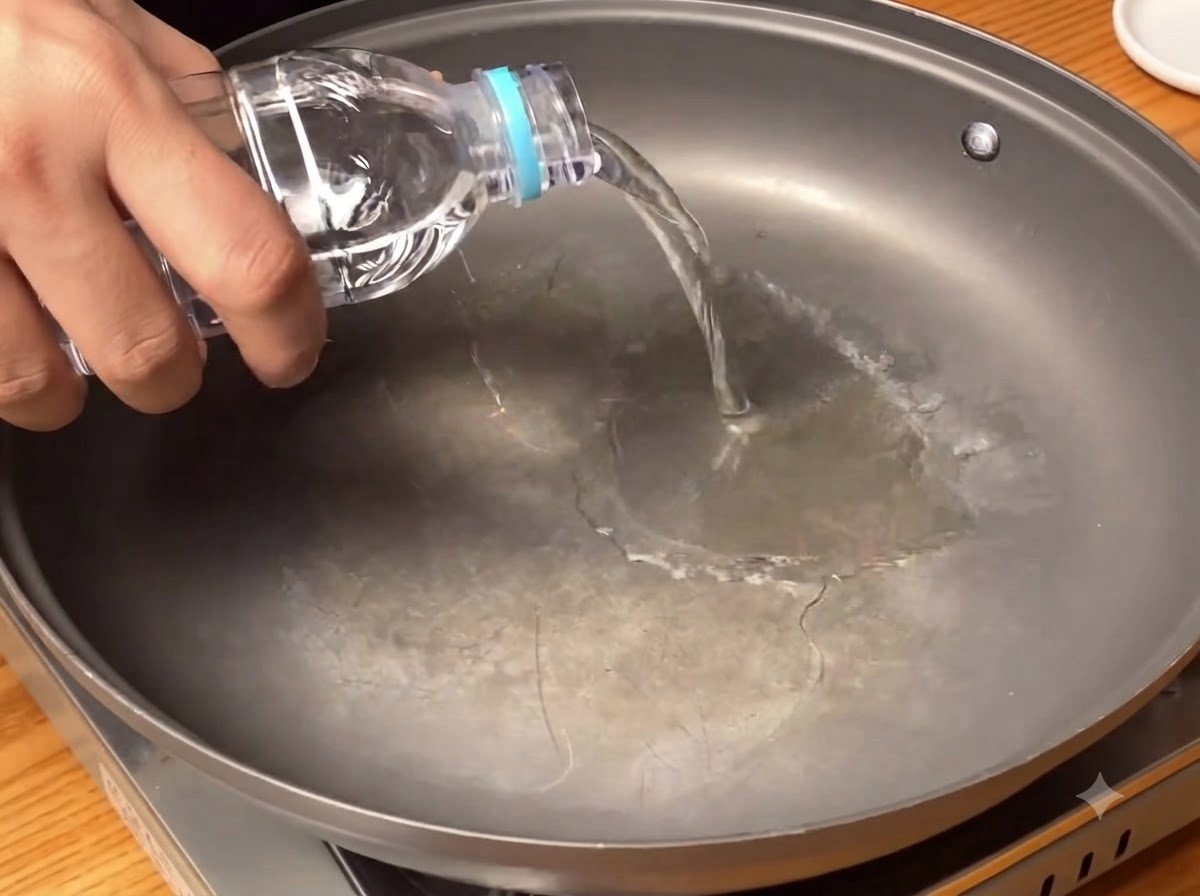 Klares Wasser wird aus einer Flasche auf den Boden einer breiten Kochpanne gegossen.
