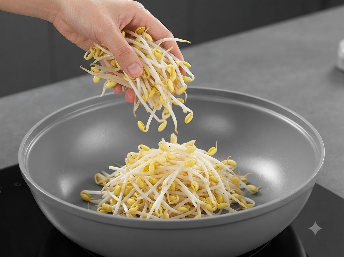 Frische Sojabohnensprossen werden aus einer Hand in die Mitte der Pfanne fallen gelassen.
