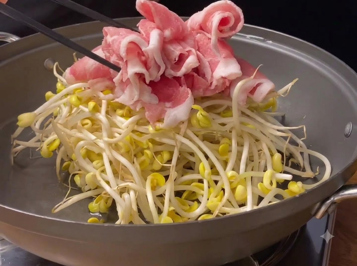 Dünn geschnittene rosa Schweinefleischrollen werden auf frischen Sojabohnensprossen in einer Kochpfanne platziert.