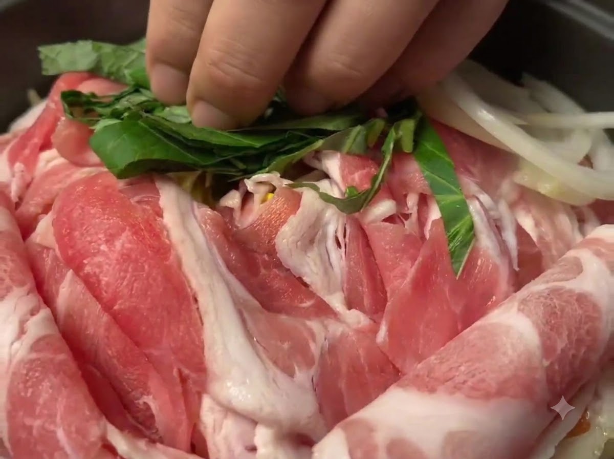 Gehackte grüne Perillablätter werden über rohen Schweinefleischscheiben in der Pfanne verstreut.