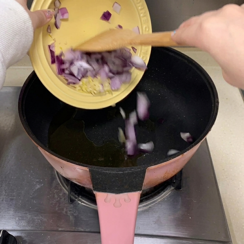 Minced garlic and red onion pieces dropping into a pan with hot cooking oil.