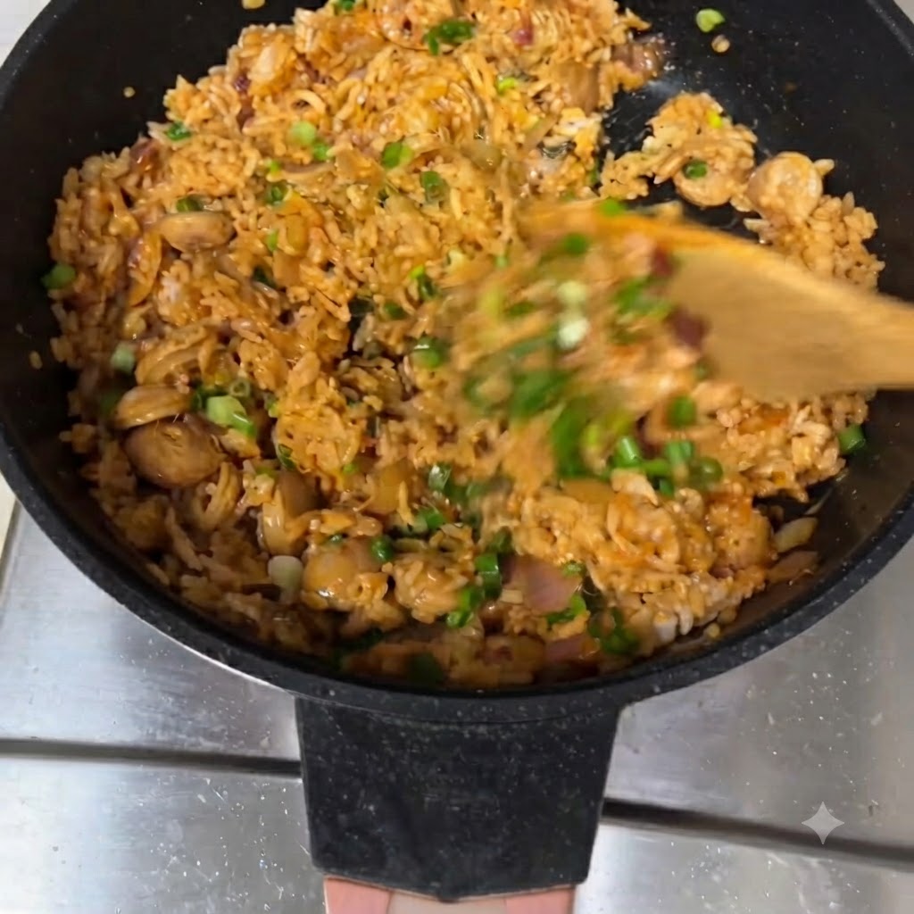 Fried rice being stirred with a wooden spatula in a pan, topped with green onions.