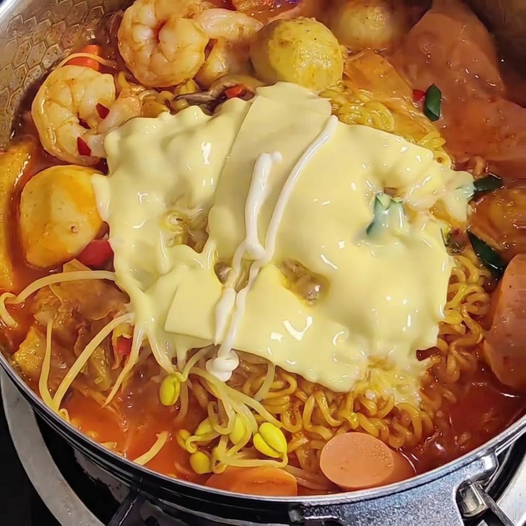 Mayonnaise wird in einem Zickzackmuster über den geschmolzenen Käse auf den Ramen gespritzt.