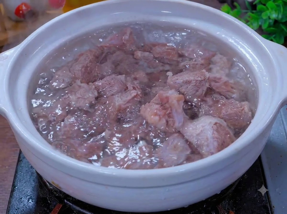 Rindfleischstücke köcheln in einem weißen Tontopf mit aromatischen Zutaten.