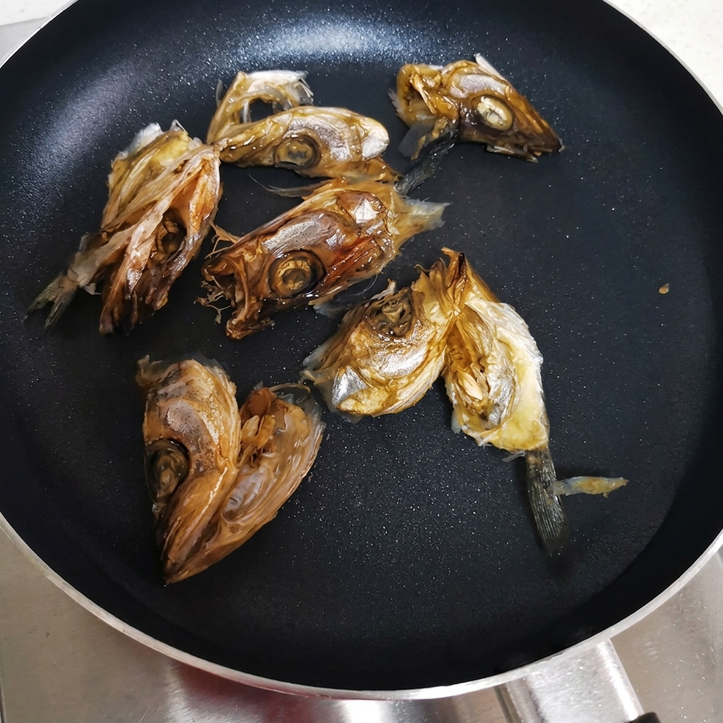 Getrocknete Fischköpfe in einem flachen Topf mit kaltem Wasser, bereit zum Erhitzen.