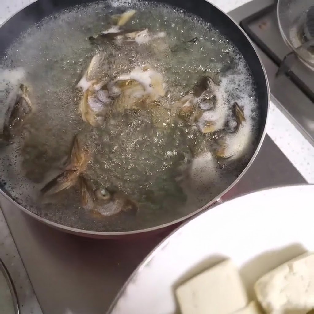 Tofuwürfel werden in einen blubbernden Topf mit Fischkopfsuppe gegeben.