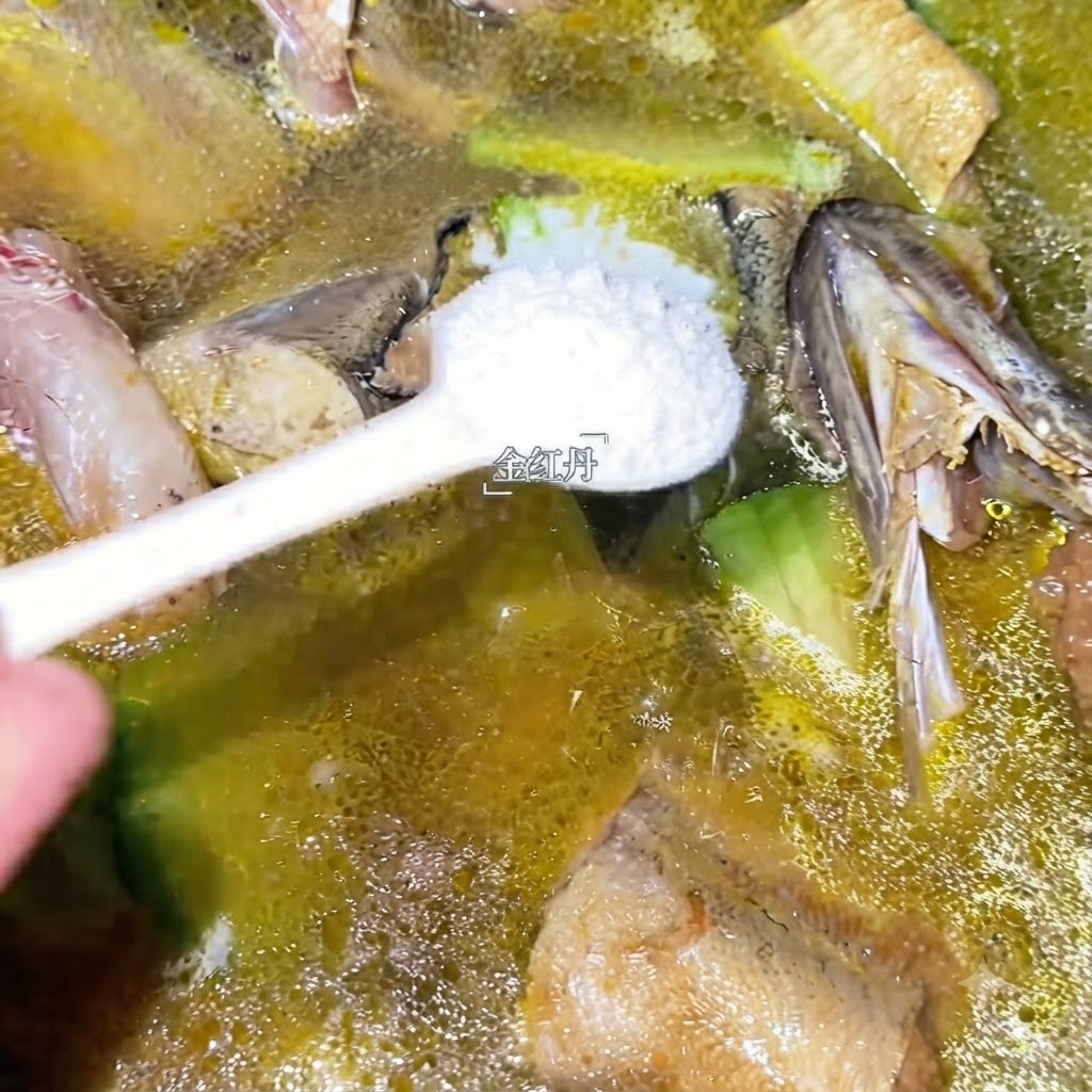 Ein Löffel weißes Gewürz wird in den köchelnden Topf mit Seelachssuppe gegeben.