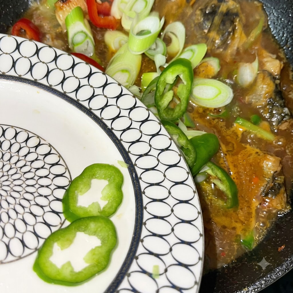 Frisch geschnittene Frühlingszwiebeln sowie rote und grüne Chilischoten werden von einem gemusterten Teller in den köchelnden Topf gegeben.