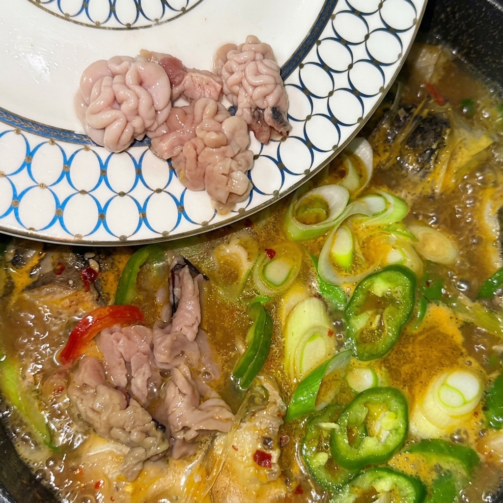 Frischer Fischmilchrogen und Fischrogen werden von einem gemusterten Teller direkt in die blubbernde Suppe gegeben.