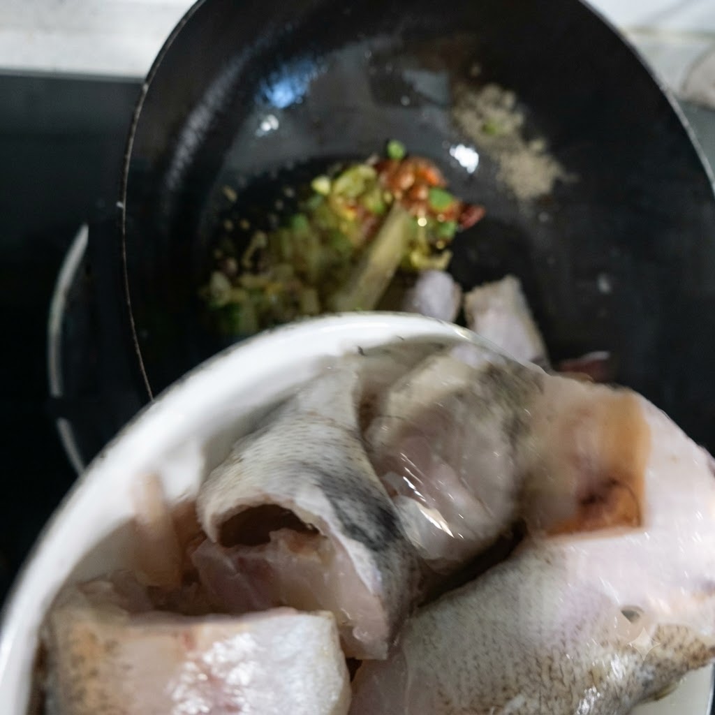 Seelachsstücke werden aus einer Schüssel in den Wok gegeben.